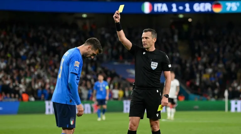 Árbitro mostrando tarjeta amarilla a jugador en partido europeo